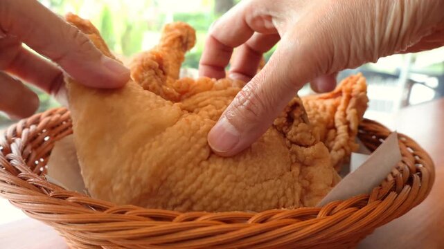 Close up POV of two hands tearing apart a crispy golden brown fried chicken showing juicy meat inside