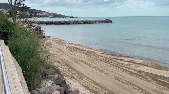 Landscape 4K view of a tractor leveling and grooming the sandy shore at a sea beach resort on a bright sunny day