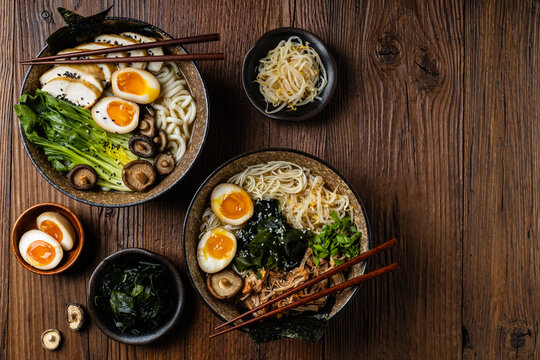 Traditional ramen with jerked pork or chicken.  With udon or ramen noodles. Served in classic bowls. Gyoza dumplings and mushrooms in the background.