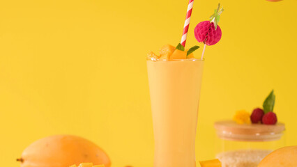 Tall Mango Smoothie Glass with Striped Straw on Yellow Background © blueringmedia