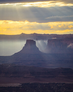 Sun rays shine over misty canyon buttes at sunrise