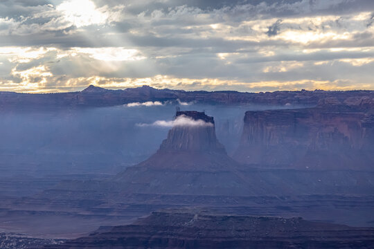 Sunbeams break through clouds above a misty canyon