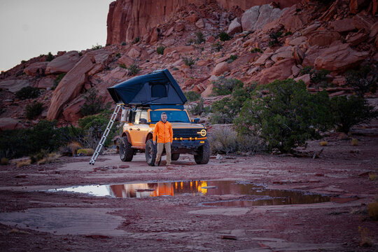 Man standing with overland vehicle and rooftop tent in a canyon