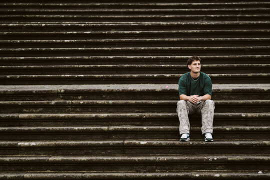 Young man sits alone thinking on wide stone steps