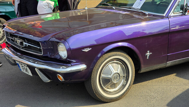 Piatra Neamt, Romania - June 7, 2025: Purple 1965 Ford Mustang showcasing its classic design, chrome bumper, distinct grille, and white-wall tires.