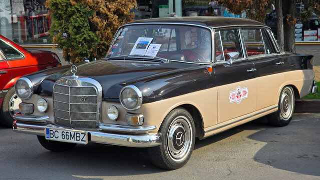 Piatra Neamt, Romania - June 7, 2025: Two-tone 1966 Mercedes-Benz W110 classic sedan, black and beige, parked outdoors. Features prominent grille, round headlights, and rally decals.