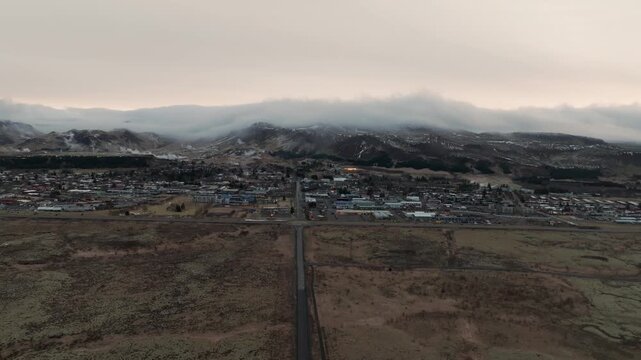 Road Through Autumn Landscape Of Hveragerdi In South Iceland, With Low Clouds Over Snow-dusted Mountains In Background. aerial pullback shot