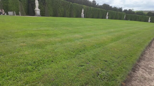 An angled shot of the Versailles Garden, with tall bush walls and statues under a blue sky.
