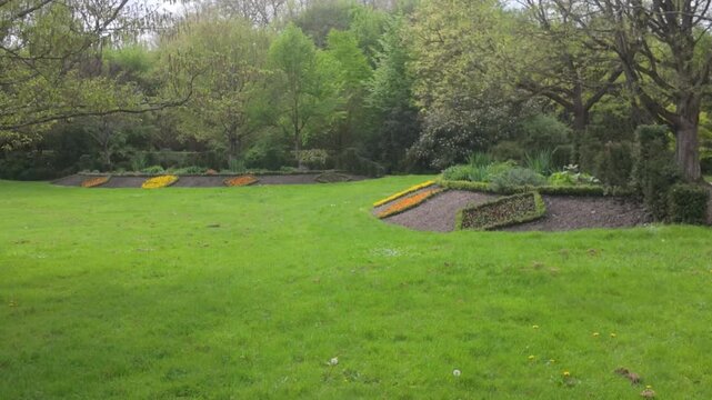 Brightly colored flowers planted at the base of trees and surrounded by green grass at Versailles.