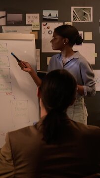 Vertical shot of African American young woman programmer explaining software development flowchart on flipchart to colleague. Clip for IT education or corporate training presentations