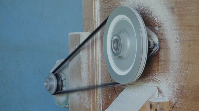 Close-up of a moving belt and pulley mechanism on a wooden flour mill, with flour dust covering the machine during grain milling.