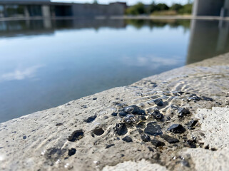 Fototapeta premium Clear water gently flowing over a textured concrete edge, reflecting modern architecture under a bright sky, capturing a tranquil, contemporary outdoor waterscape