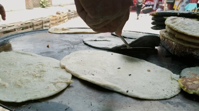 Closeup view of street food vendor preparing fresh quesadillas on hot metal griddle at busy outdoor market during daytime with traditional cooking process and local cuisine