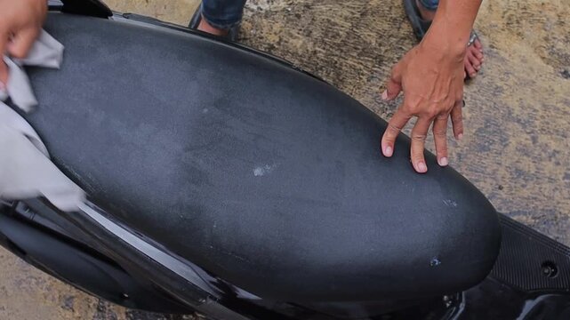 Close up of man hands carefully applying polish to black leather motorcycle seat outdoors