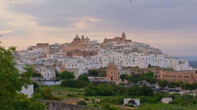 Ostuni, Brindisi Province, Puglia, Italy, featuring whitewashed historic architecture, Ostuni Cathedral, medieval streets and rolling olive groves beneath soft sunset light establishing landscape shot