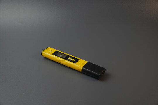 Yellow digital pH meter tester pen isolated on a dark grey background. Portable electronic device for measuring acidity or alkalinity in water quality control, laboratory, and hydroponics.