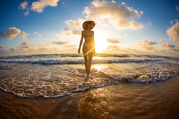 Fototapeta premium Slender girl having fun in the sea and her legs are washed by ocean waves. young girl on the beach.