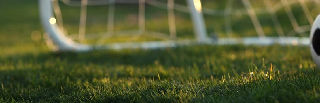 Soccer ball bouncing on grass near goal net at sunset