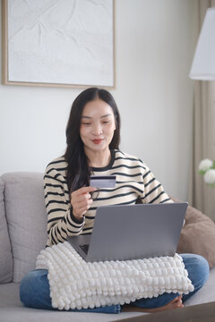 Young woman shopping online with a laptop while holding a credit card at home, representing e-commerce, digital payment, and online banking.