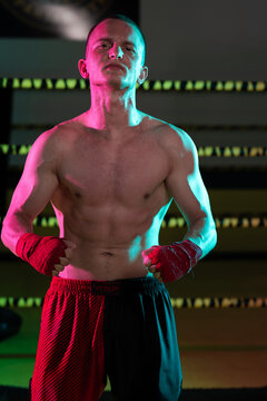 Confident Male Boxer With Hand Wraps Posing in Gym Under Dramatic Colored Lighting
