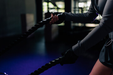 Cropped shot of woman hands gripping battle ropes during intense strength training session at gym, focusing on fitness, power, determination through vigorous exercise. © dikushin