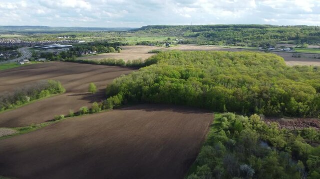 Aerial view of Milton, Ontario, Canada as shot from a drone on a mixed sunshine and clouds spring day in May, 2022. Flying southwest towards Bronte and the Escarpment over fields and trees.