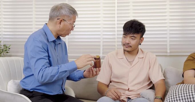 Asian senior therapist demonstrates medication bottle to adult man during counseling session, explaining treatment plan for depression and stress management, calm communication and trustful atmosphere