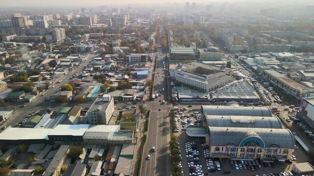 Drone flyover along a busy urban avenue in Bishkek, Kyrgyzstan, passing the Osh Bazaar district and surrounding commercial neighborhoods.