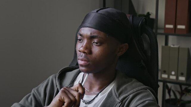 Chest-up shot of African American man sitting in office chair, twirling stylus pen and looking thoughtfully at computer screen. Clip for videos about software development, IT startups, and coding