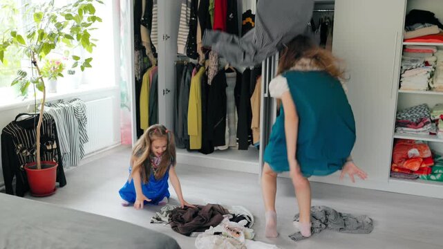 Cheerful sisters throwing wardrobe clothes high into bedroom atmosphere.