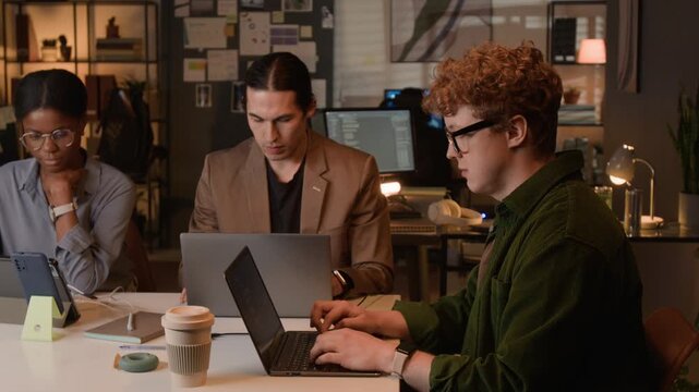 Multiethnic young programmers working on laptops and collaborating in office at night. Footage for software development commercials and tech startup marketing campaigns