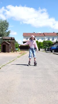 Generation Alpha girl riding inline roller skates on suburban asphalt street. Female child wearing pink hoodie and denim jeans skating outdoors on sunny day. Full length view of rollerblader balancing