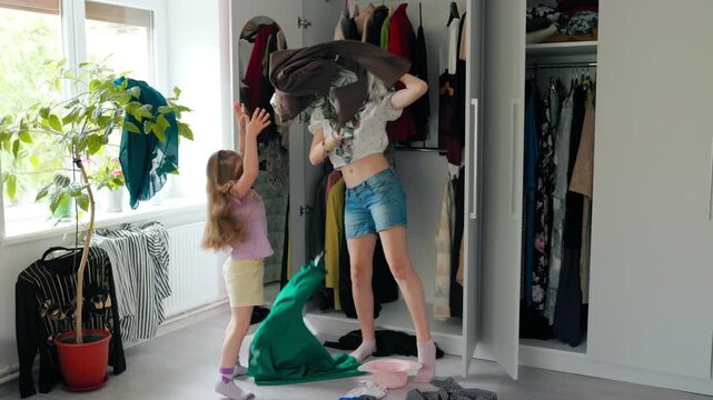 Young kid playfully throwing clothes while tween sister dances.