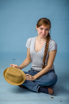 Young woman sitting on floor with a straw hat in a blue background  