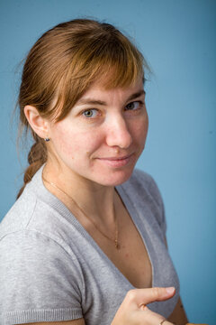Woman with brown hair smiling while holding a pencil against blue background  