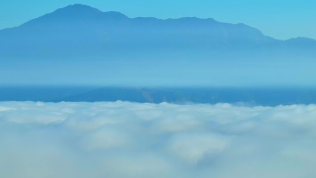 Drone aerial view of forests blanketed in mist with mountains in the background, illustrating carbon storage, biodiversity support and climate regulation provided by forests. Southeast Asia, Thailand.