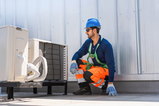 Technician inspecting air conditioning units outdoors, Professional HVAC technician checking air conditioning condenser unit on rooftop during maintenance