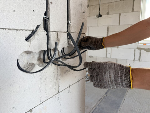 electrical wiring in a new building. A male electrician installs an electrical cable into the wall of a new building. Construction and repair