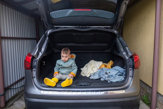 Toddler Sitting in Open Car Trunk in Garage.