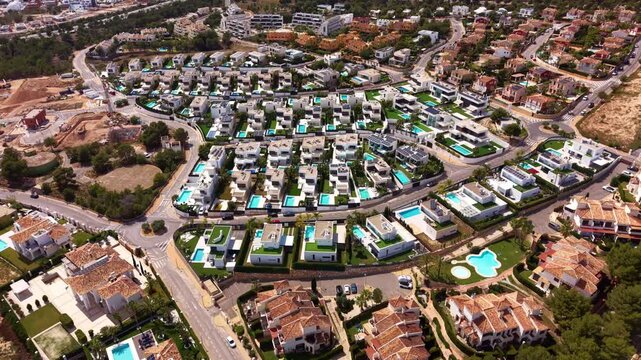 Overhead view of a Spanish coastal residential neighborhood with modern white villas, private swimming pools, terracotta rooftops, and winding streets surrounded by Mediterranean vegetation