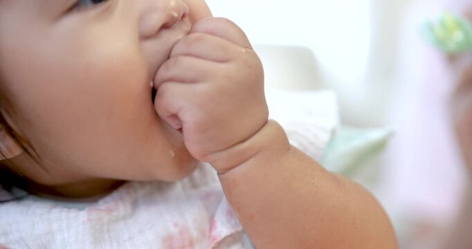 Close up Asian toddler girl biting small piece of grape with chubby hand, focused expression, warm daylight on skin, cozy living room, early self feeding, child development and sensory learning moment