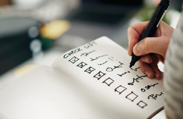 Close Up of Hand Using Black Marker to Check Off Items on Grid Notebook Checklist