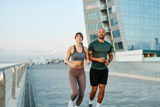 Couple jogging along waterfront pathway at sunset creating a healthy lifestyle