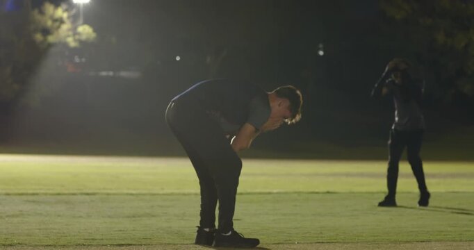 After match white teenage male bowler walking and shaking umpire hand under floodlights