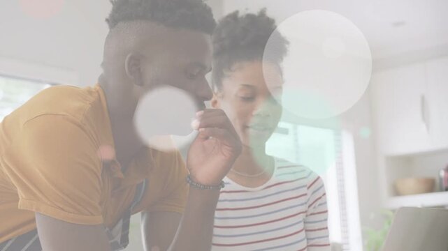 Couple leaning at kitchen counter using laptop, tapping trackpad showing overlays for tech planning