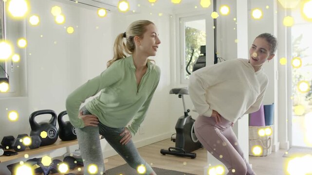 Two women smiling hands-on-hips doing synced side lunges for fitness, yellow particles marking form