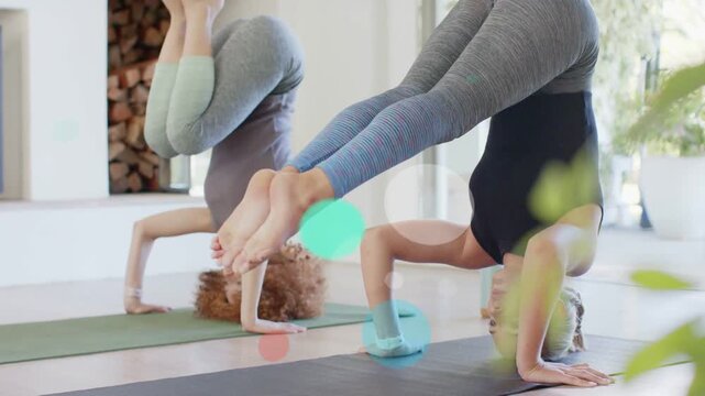 Two women starting forearm pose in yoga studio, lifting legs for balance while bokeh crossing frame