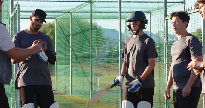 Male coach adjusting vest before delivering batting tips to trainees at cricket net