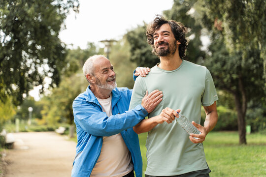 Senior man having fun doing sport in the park together with young son, talking and supporting each other 