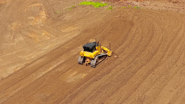 Industrial bulldozer grading land and pushing earth with front blade across development area. Overhead construction machinery highlighting earthworks, terrain preparation, large scale engineering